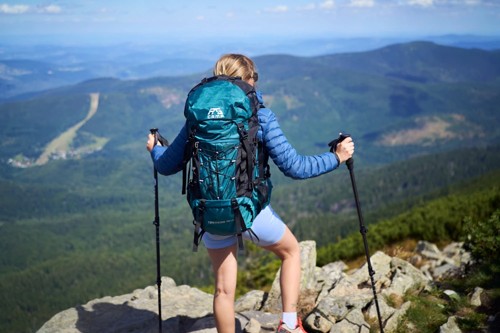 Kobieta z plecakiem turystycznym i kijkami trekkingowymi w górach
